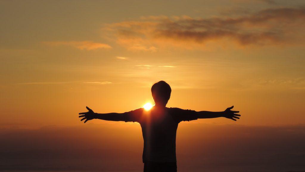 a man standing in front of the sun with his arms outstretched